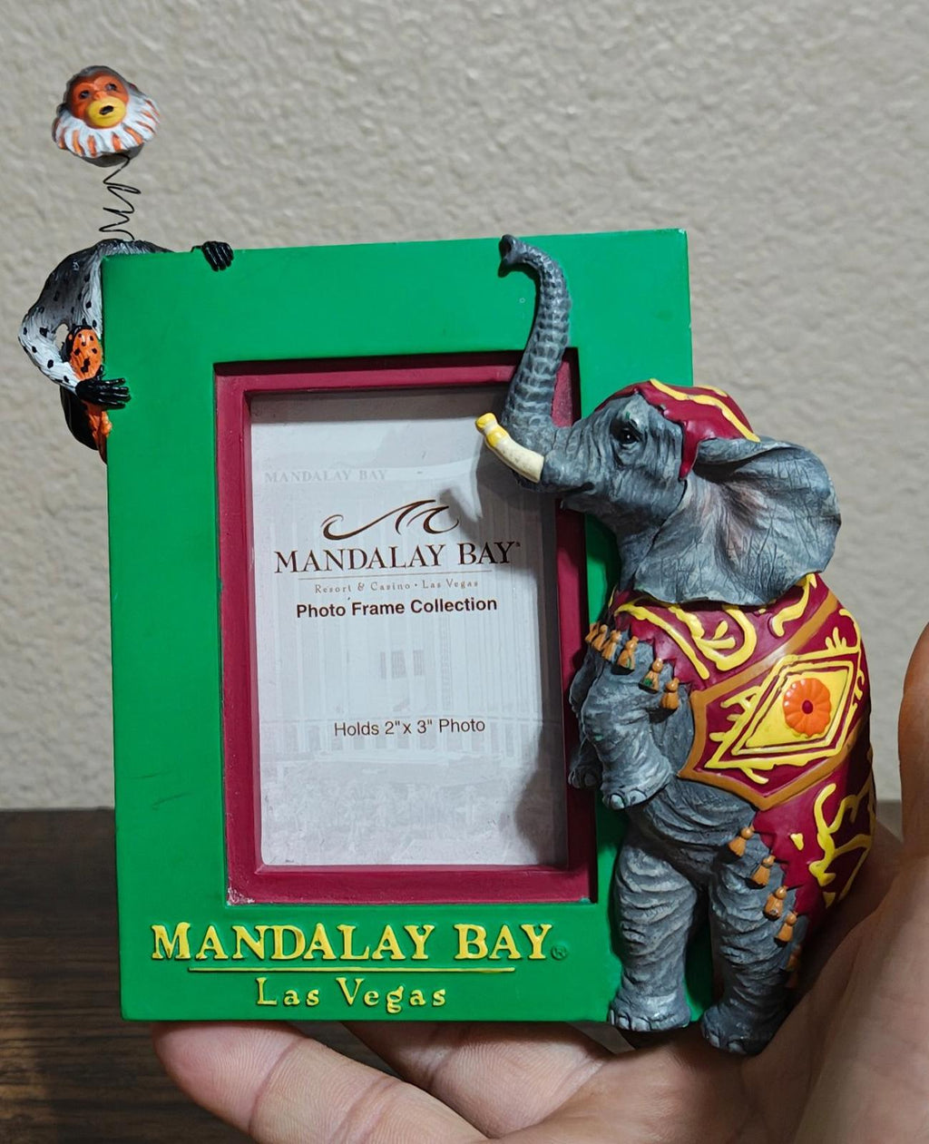 Green souvenir photo frame featuring an elephant carrying a monkey, front view