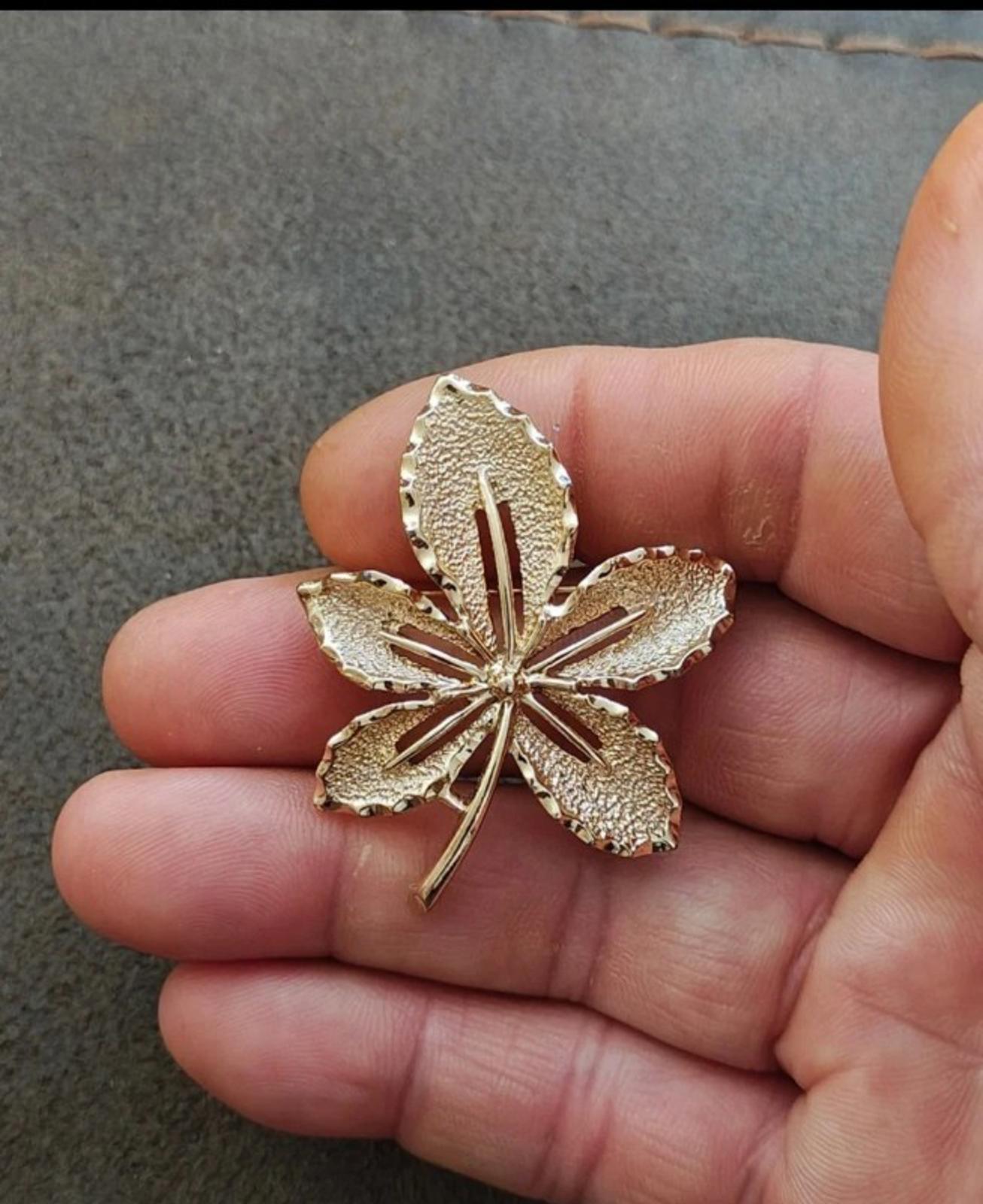 Gold-tone leaf flower brooch held in hand; five leaves with central stem detail