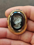 Oval cameo brooch with gold-tone frame, black background, silver profile figure in relief