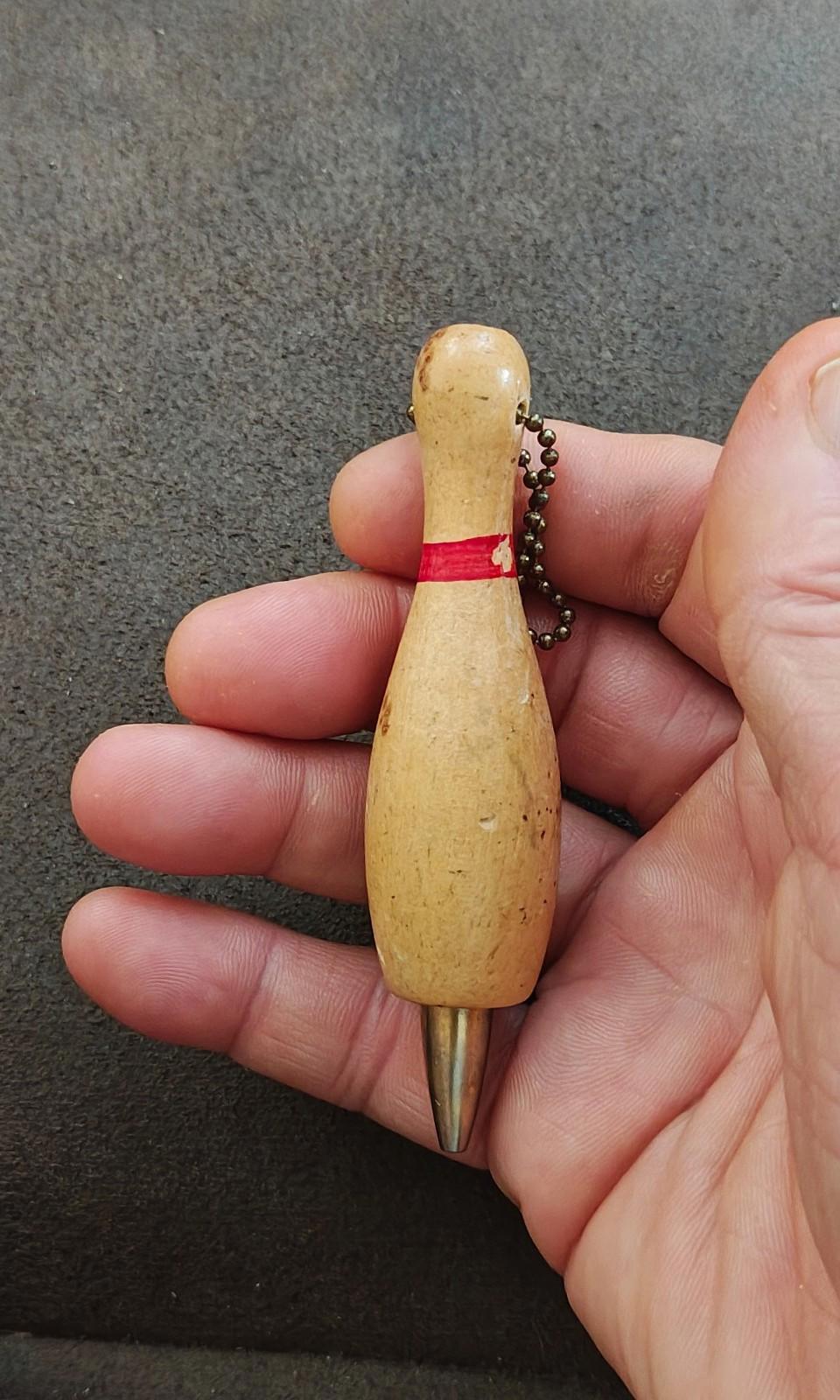 Beige wooden bowling pin mechanical pencil keychain held in hand with red band and chain