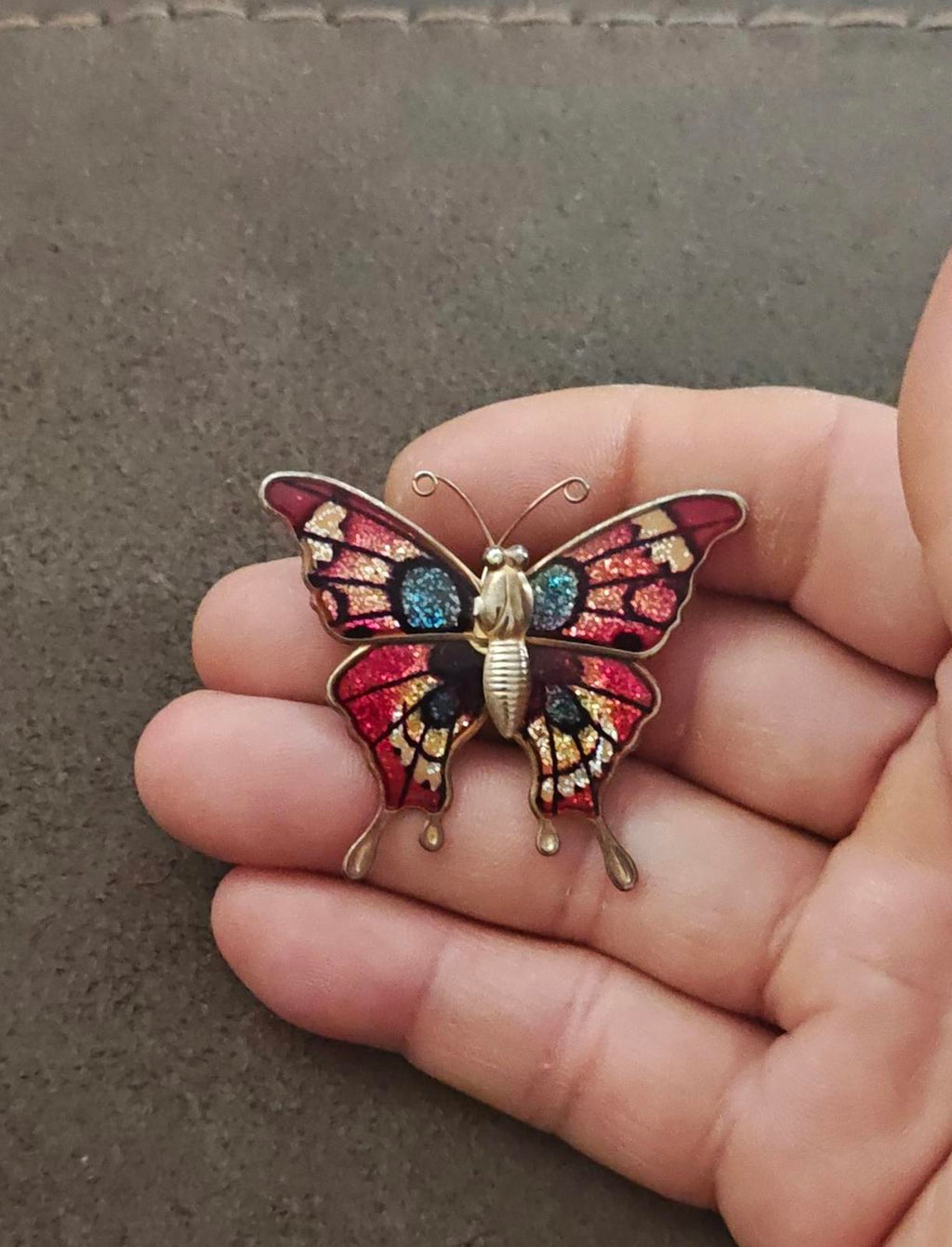 Butterfly brooch in palm, red enamel wings with blue sparkle accents and gold-tone legs