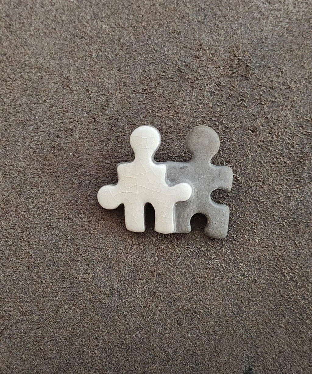 Two-piece puzzle buddy brooch on dark felt: white and gray joined figure shapes