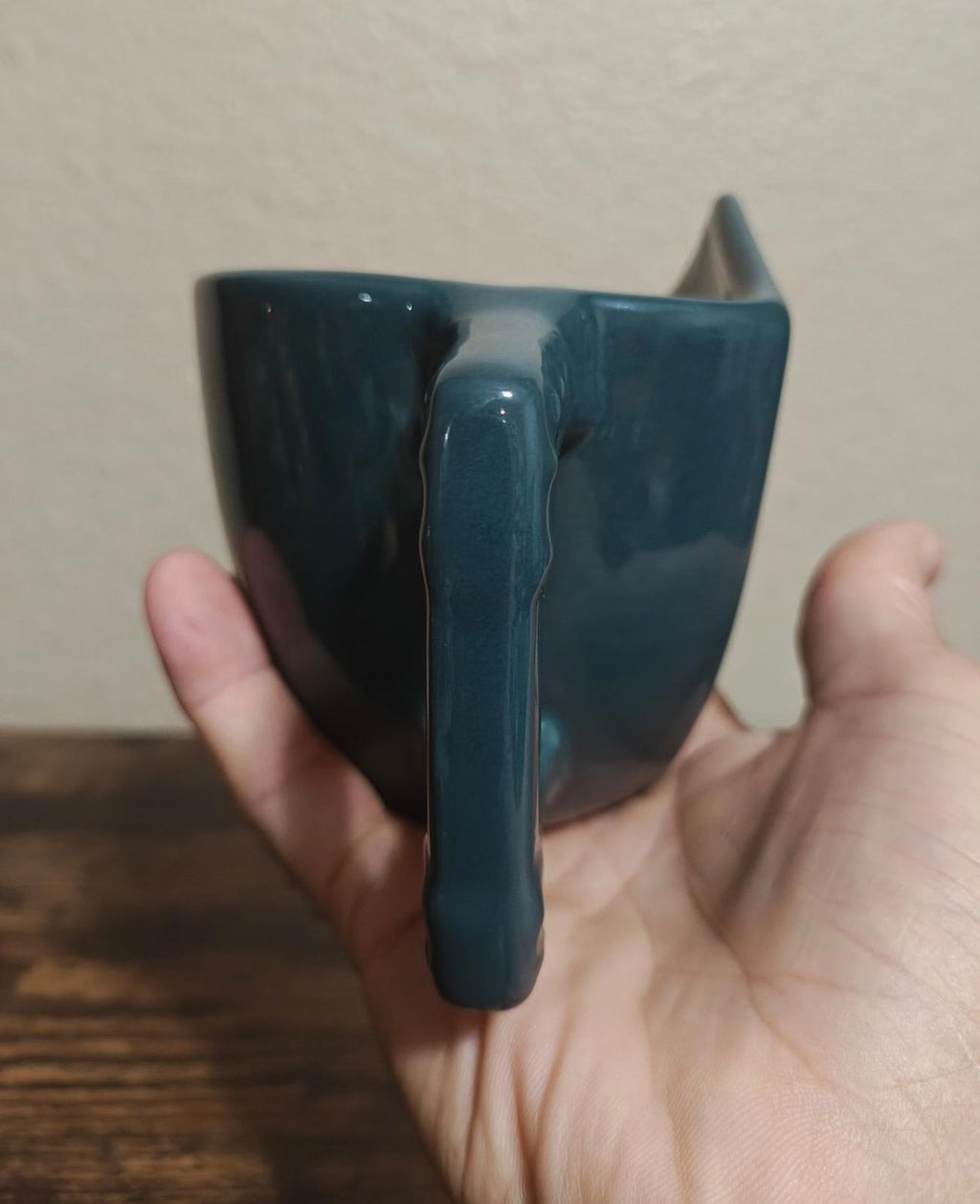Blue ceramic mug with claw-like handle and pointed spout, side view.