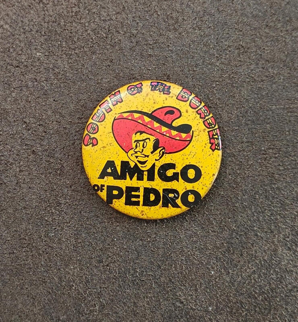 Centered yellow AMIGO OF PEDRO pinback button with sombrero mascot graphic on gray surface