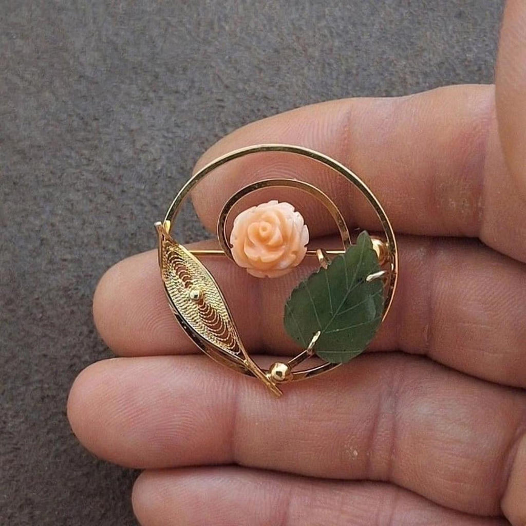 Gold-tone circular filigree brooch showing pale rose cabochon and green leaves.