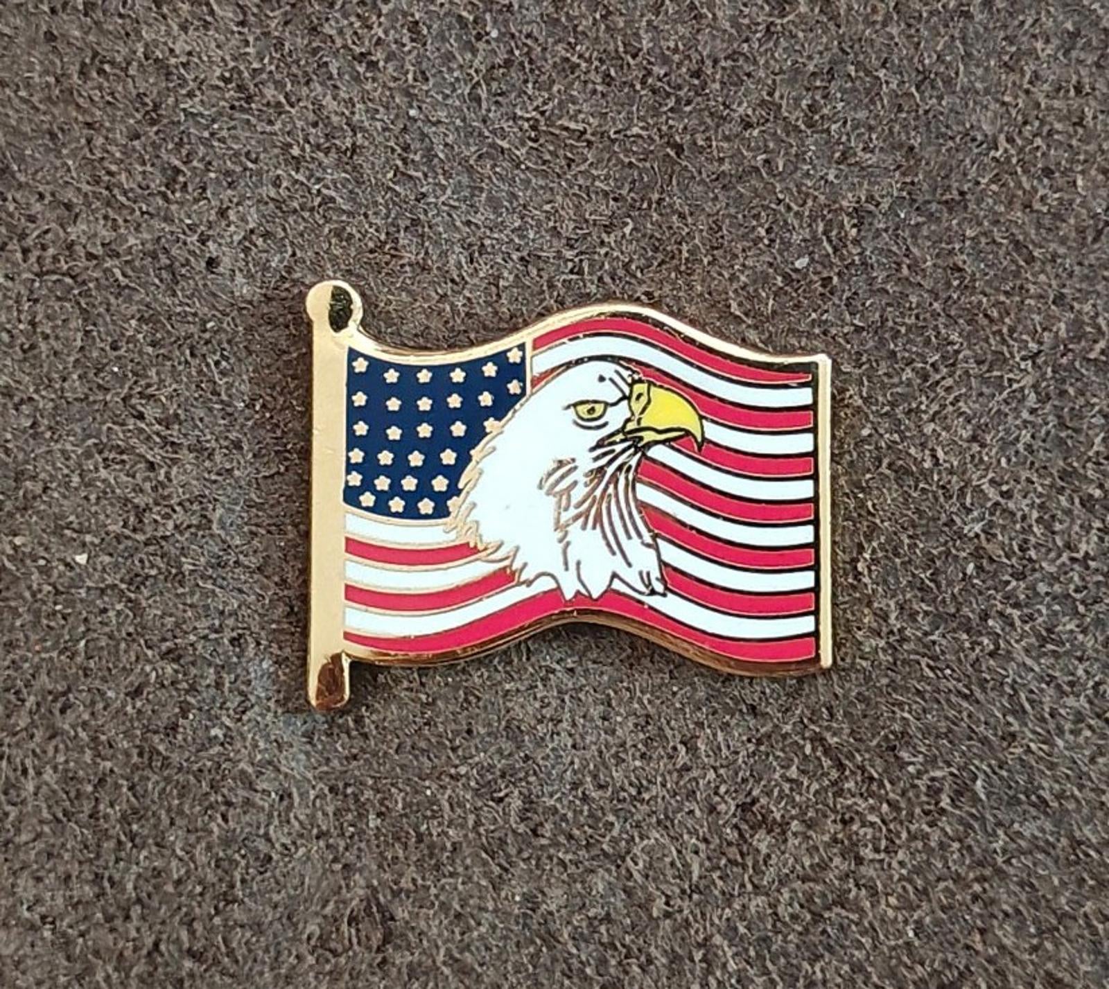 Gold-tone enamel wavy American flag lapel pin with bald eagle, front view on surface