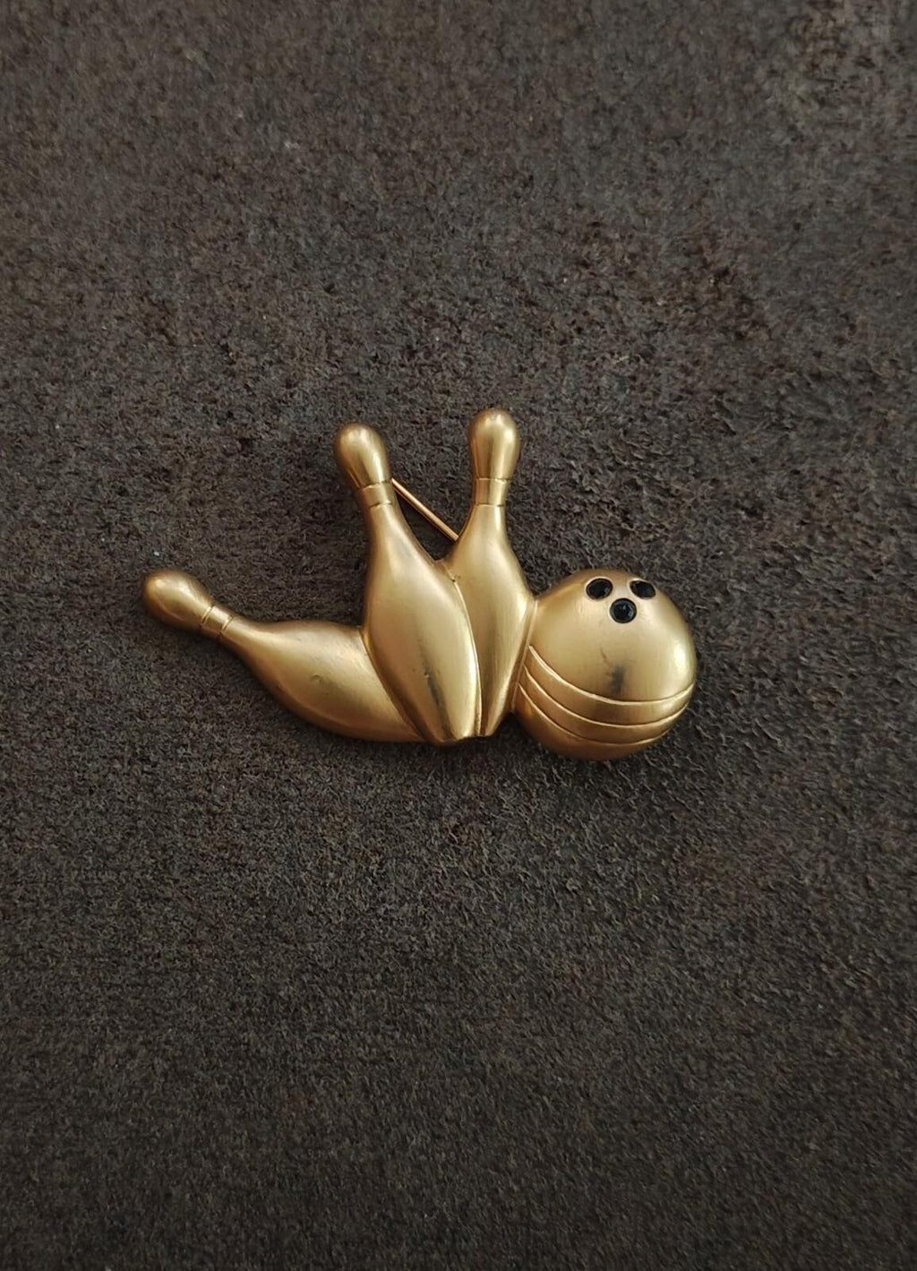 Gold-tone bowling pin and ball brooch on dark background, small profile