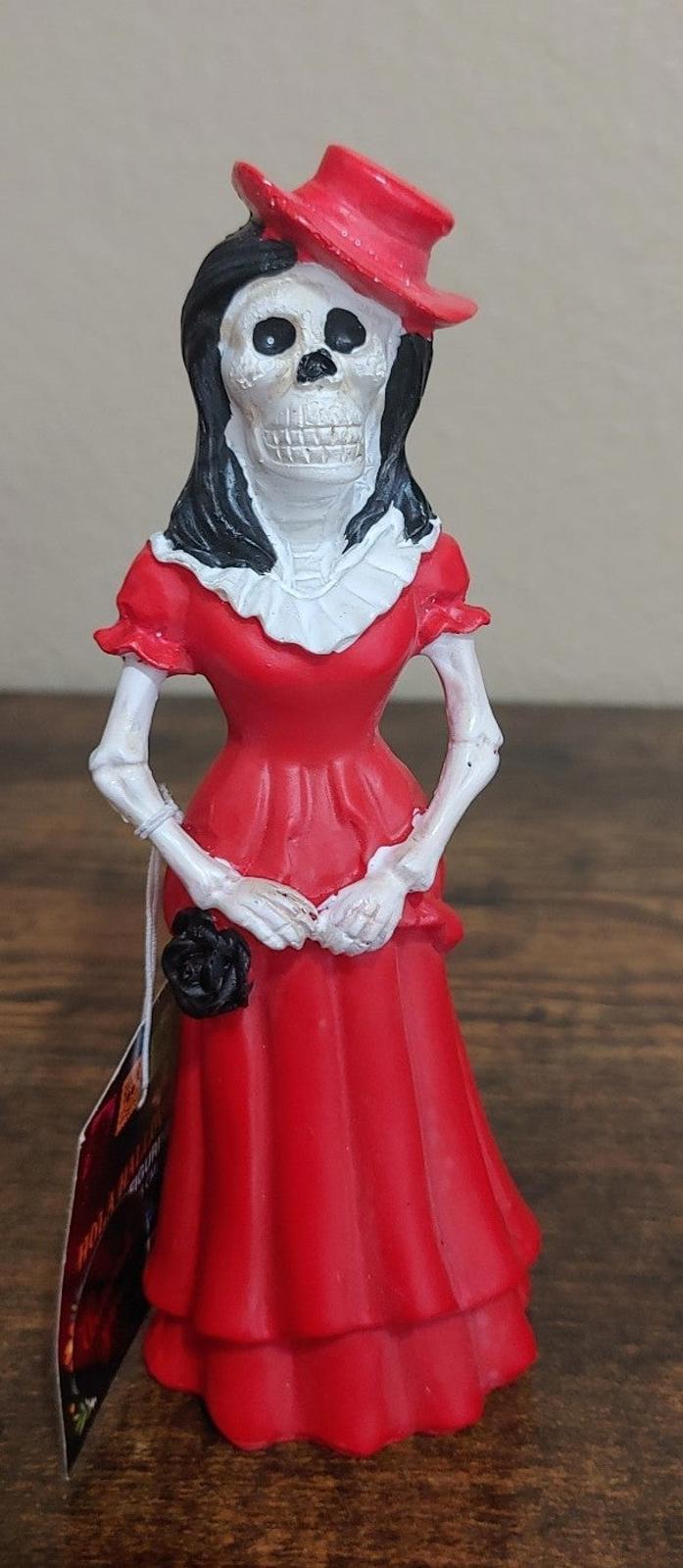 Red Catrina figurine with black hair and white skull face, festive hat