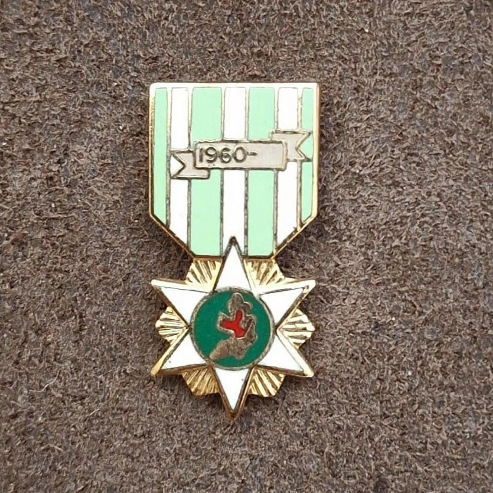 Green-and-white striped enamel campaign pin with starburst frame and red emblem.