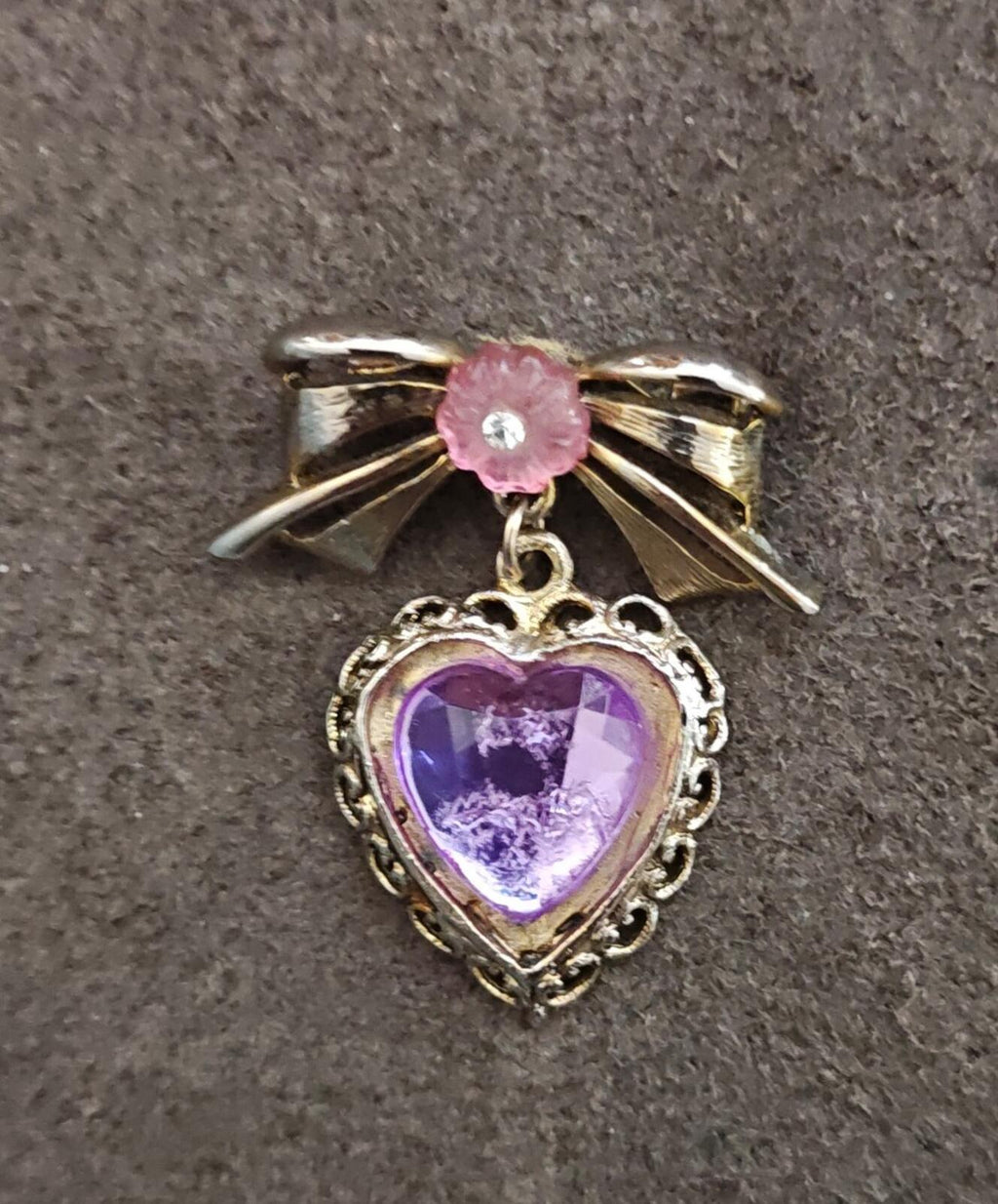Close-up gold-tone heart brooch with purple stone heart and pink flower accent bow