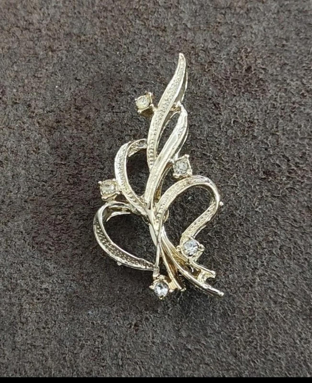 Gold-tone ribbon brooch featuring looping vine arms and scattered rhinestone accents