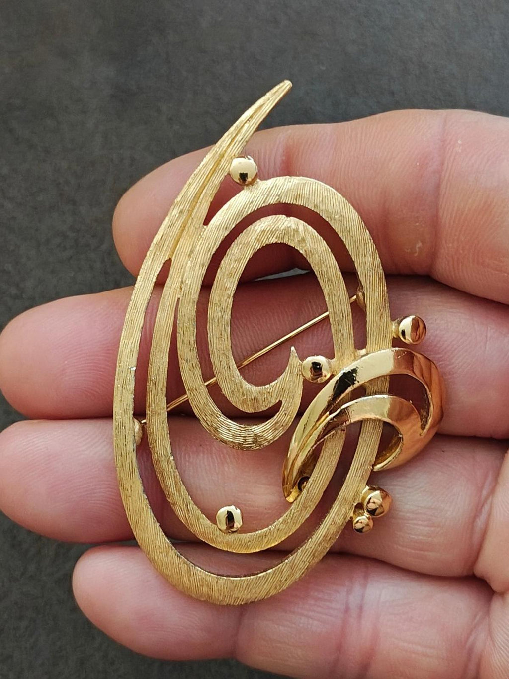 Gold tone oval brooch pin with double swirl design and pin clasp on the back