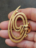 Gold tone oval brooch pin with double swirl design and pin clasp on the back