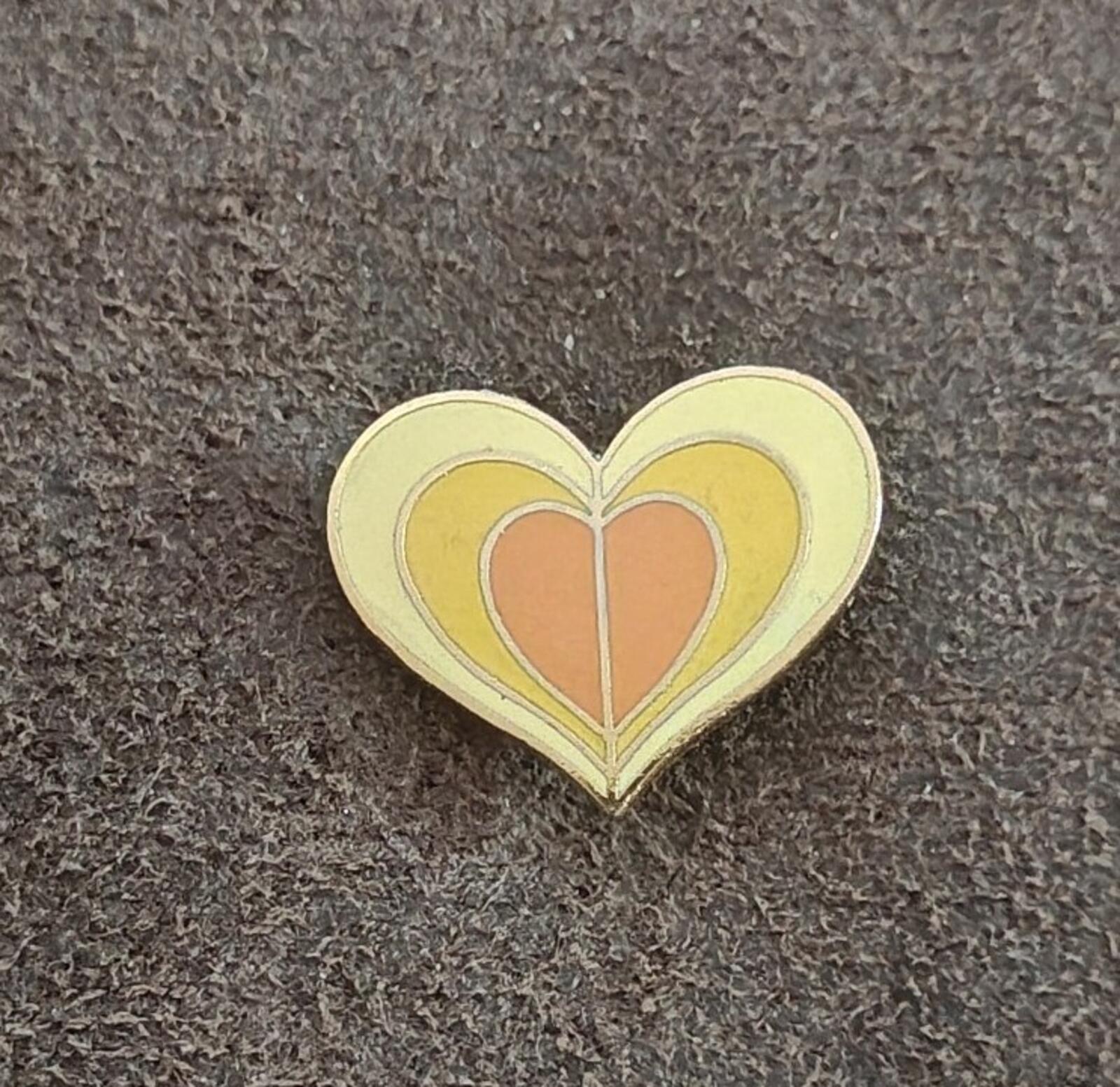 Enamel heart pin showing layered yellow rings and an orange heart motif.