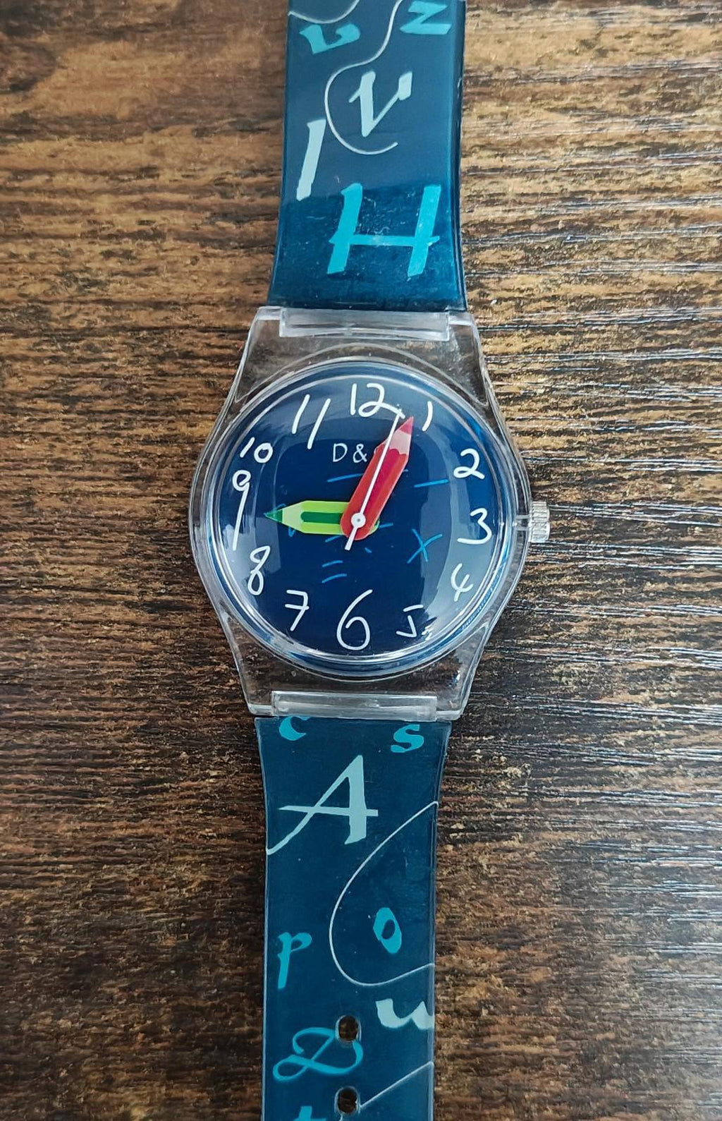 Blue unisex teacher watch with round blue dial, red hands, and printed number/letter strap