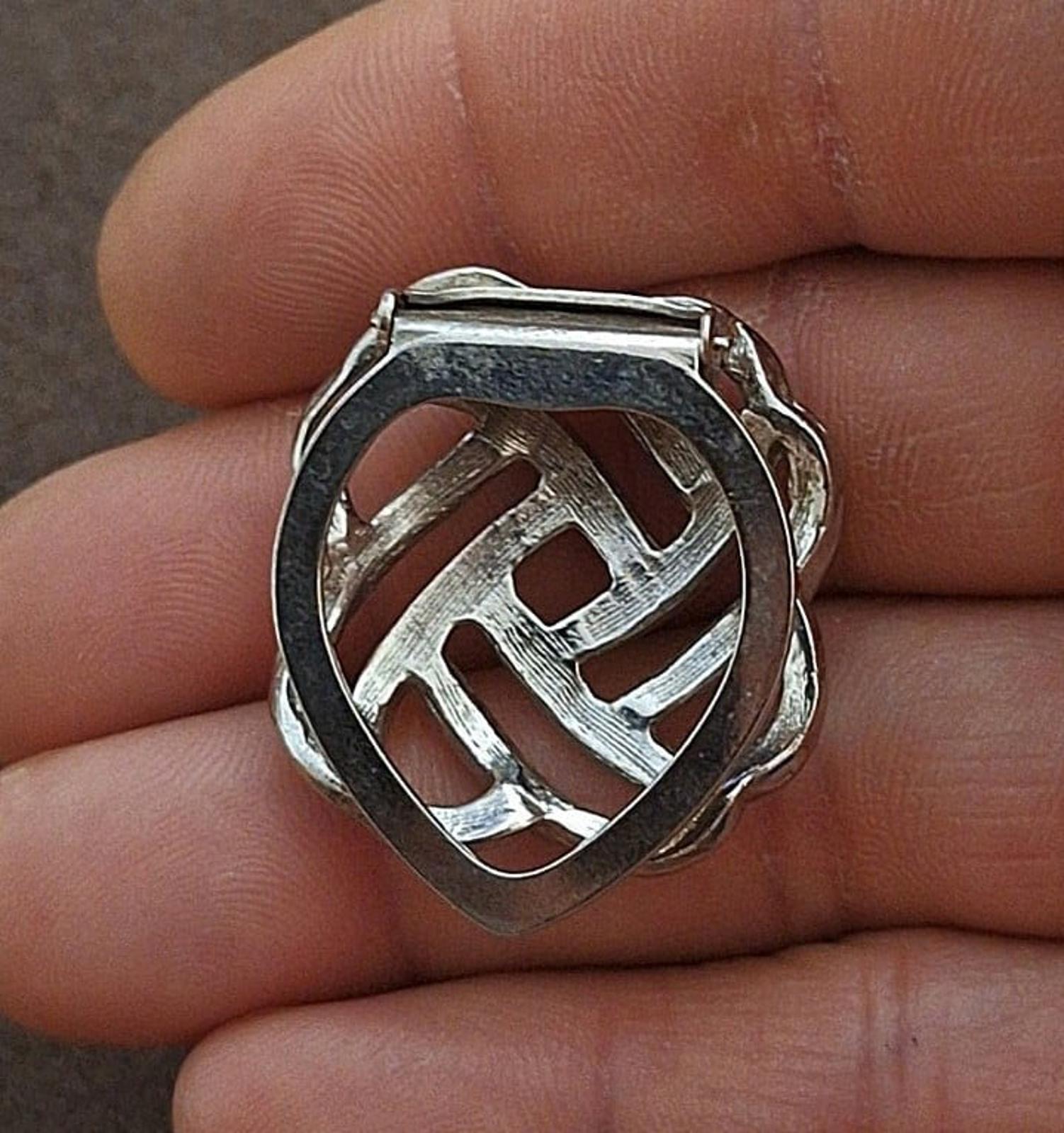 Silver scarf clip back with lattice cutout and hinge clasp, held in fingers