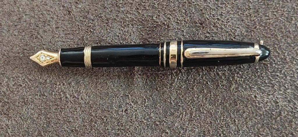 Fountain pen brooch with black enamel body, gold-tone bands, and clear rhinestone tip.