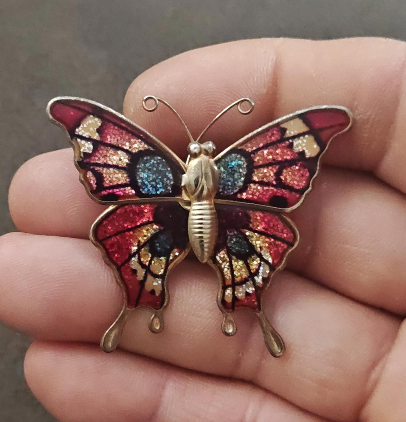Butterfly brooch held in hand, red enamel wings with blue glitter accents and gold-tone detail