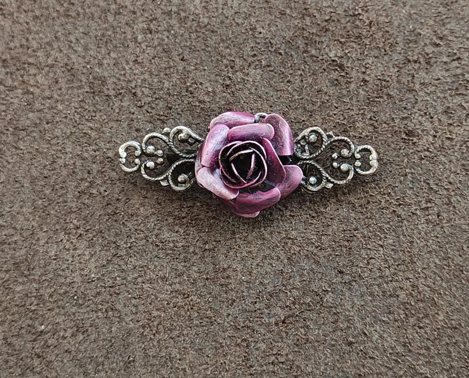Purple rose centerpiece brooch with silver filigree side scrolls on a gray background