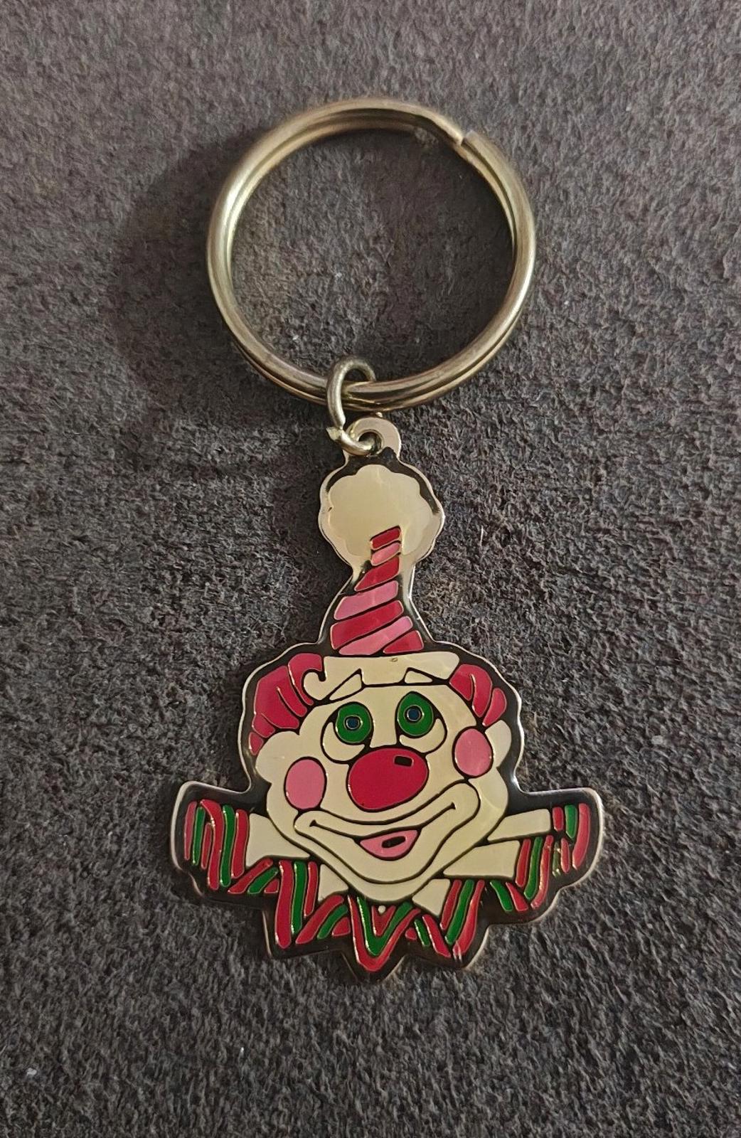 Gold-tone ring keychain with multicolor clown face charm on dark carpet