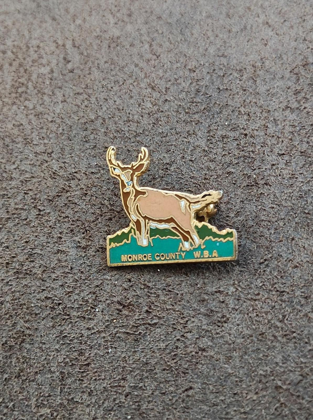 Gold-tone deer enamel pin with green base and text Monroe County W.B.A.