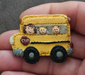 Yellow school bus resin pin with cartoon kids, black wheels, and red STOP sign
