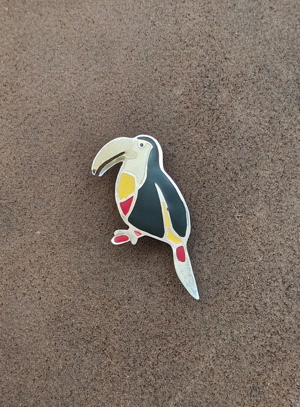 Toucan bird enamel brooch, shown flat on surface; black wings with yellow and red details.