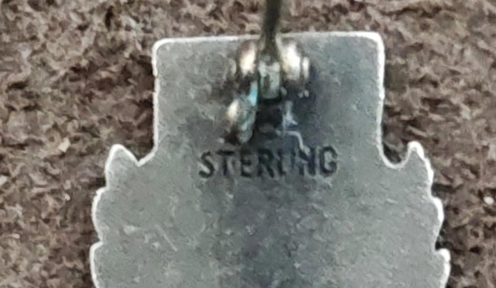 Close-up of silver pin back with stamped lettering in the center