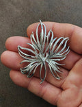 Silver tone leaf pin brooch with frosted detail, held on fingers, close-up view