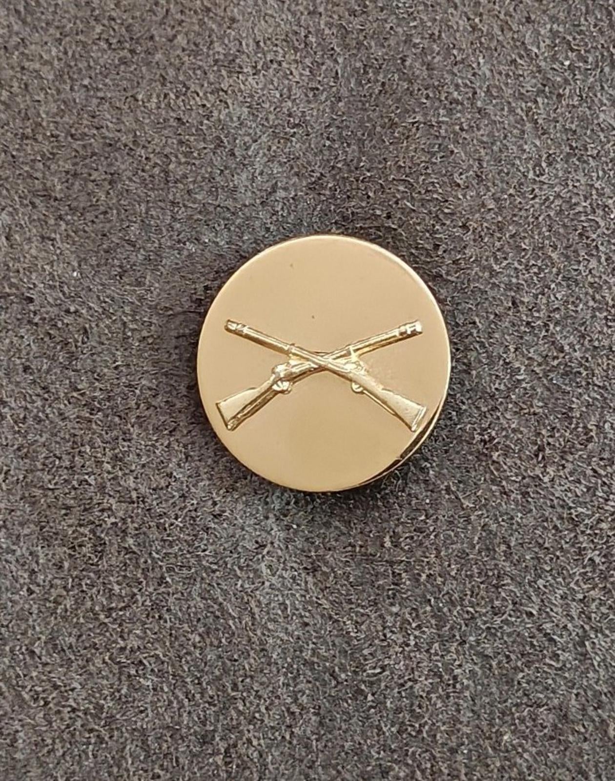 Gold circular brass pin with crossed rifles emblem, front
