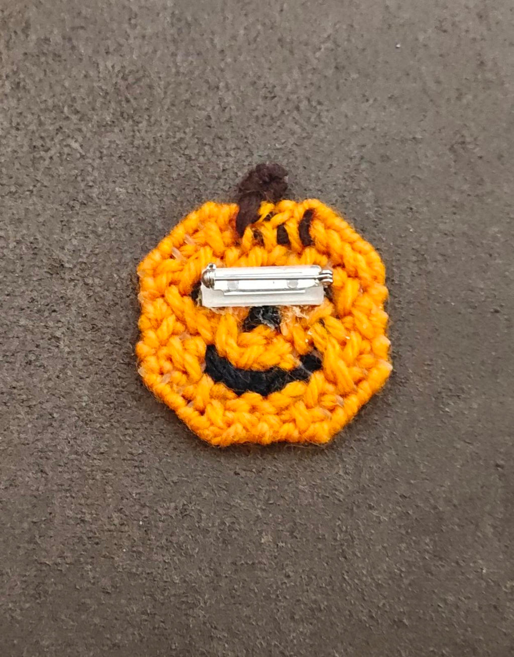 Orange jack o' lantern brooch back view showing silver pin and black stitched face.