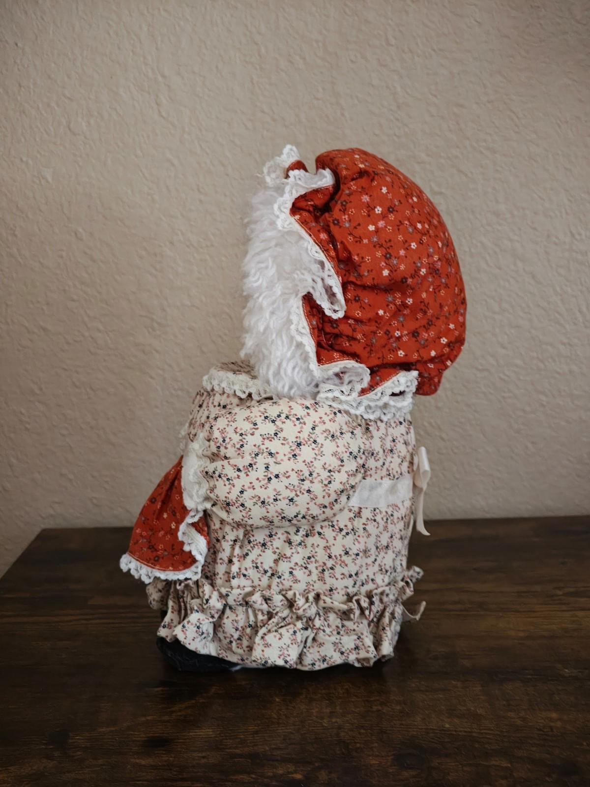 Handmade cloth doll canister from the back, red bonnet and white floral dress with ruffles.