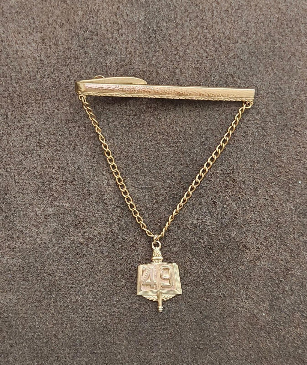 Gold-tone tie clip with chain and hanging book charm marked 49