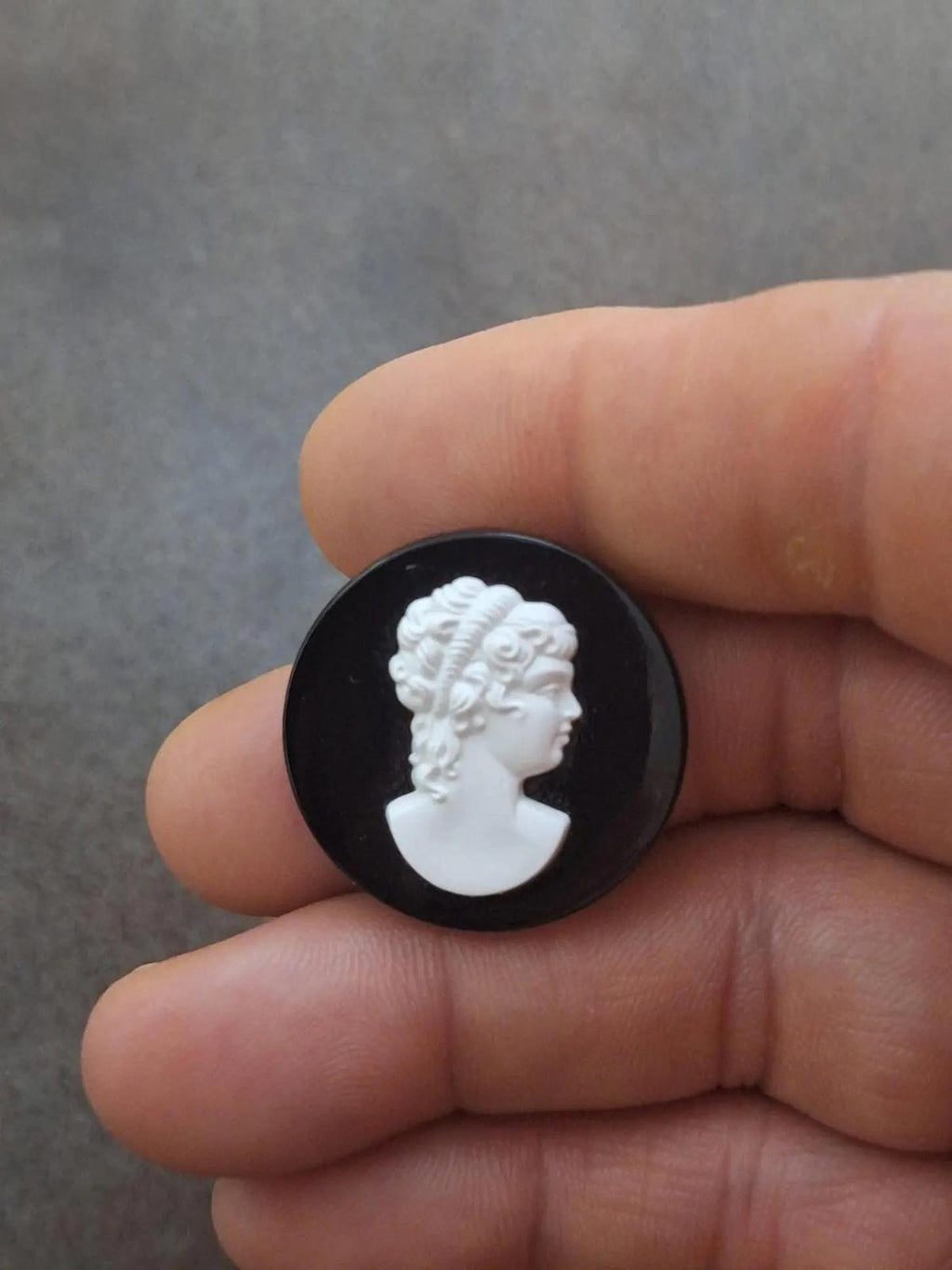 Black round cameo brooch held in fingers with white woman profile relief