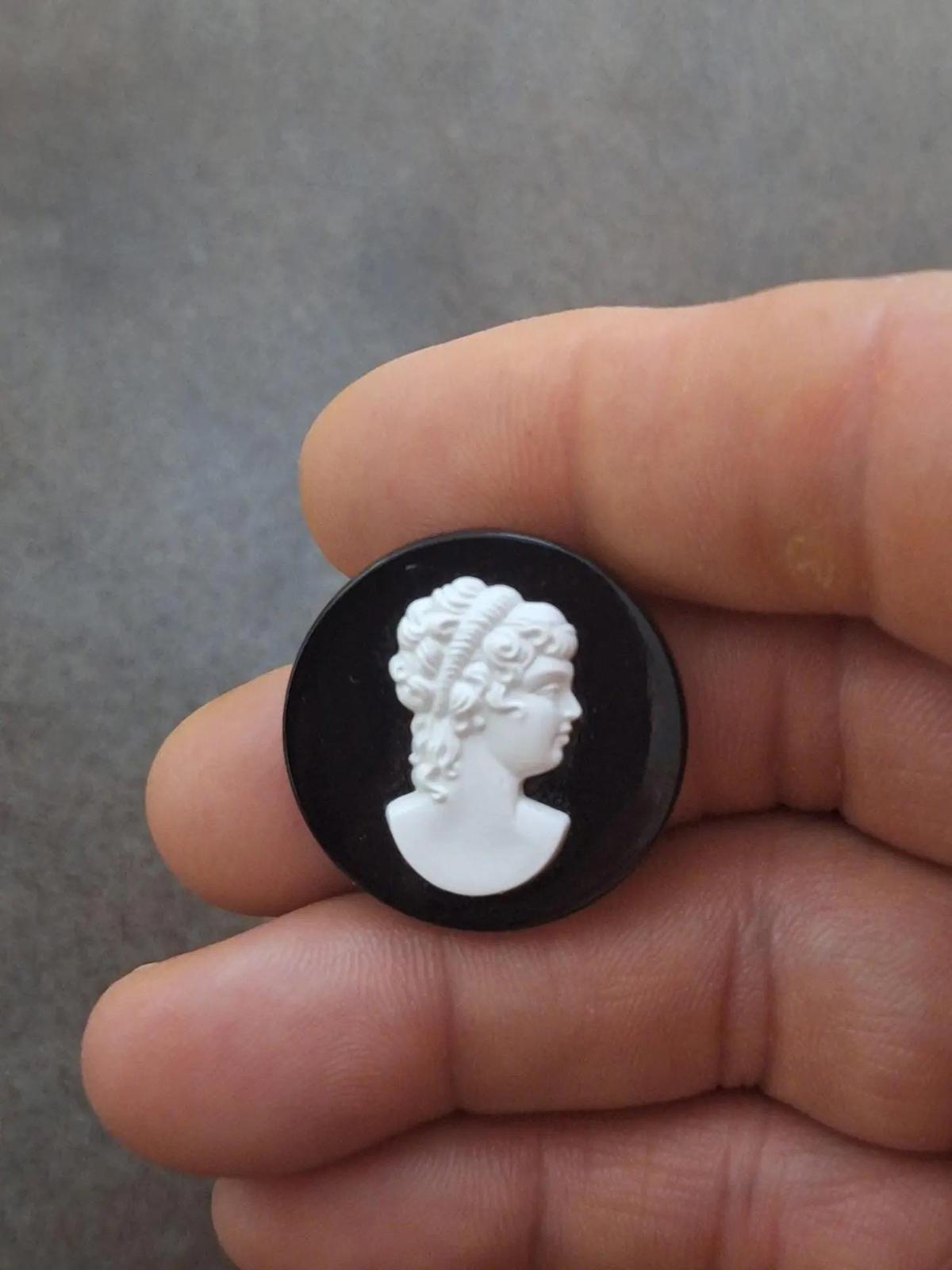 Black round cameo brooch held in fingers with white woman profile relief
