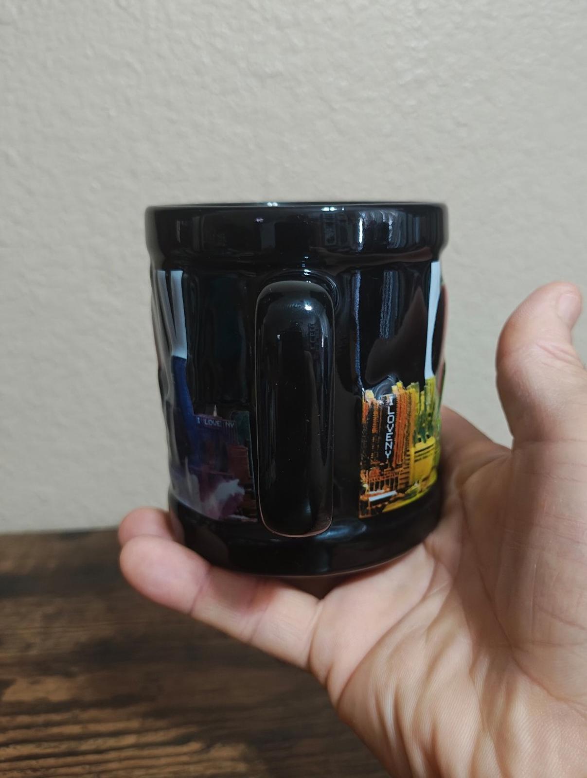 Black ceramic mug with colorful skyline graphic, glossy glaze, rear-side angle