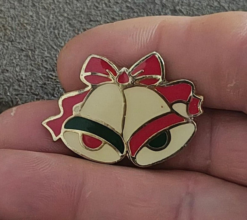 Gold tone enamel Christmas bells brooch with red ribbon and green accents, close-up on hand
