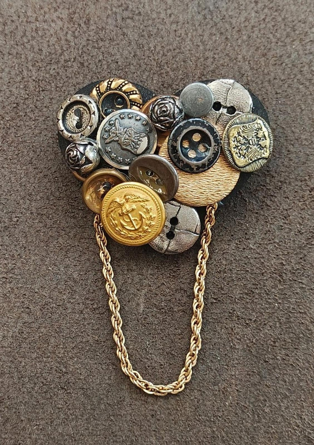 Button collage brooch with gold-tone chain and tan fabric backing, mixed metal button design