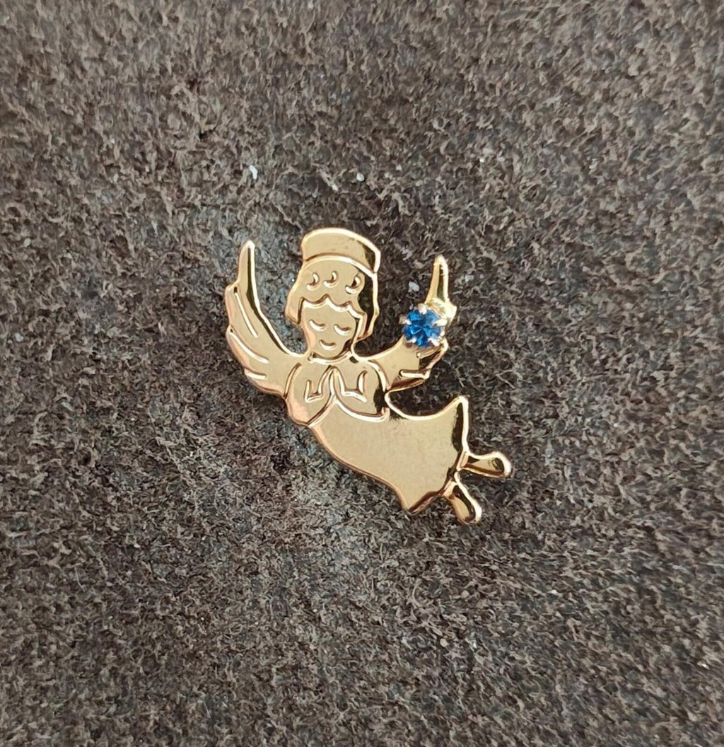 Gold angel lapel pin with blue rhinestone on textured gray background