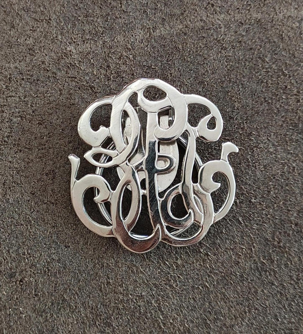 Silver-tone monogram scarf clip, close-up view of raised ornate letterwork