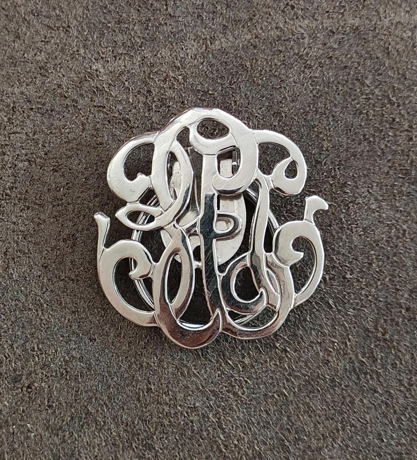 Silver-tone monogram scarf clip, close-up view of raised ornate letterwork