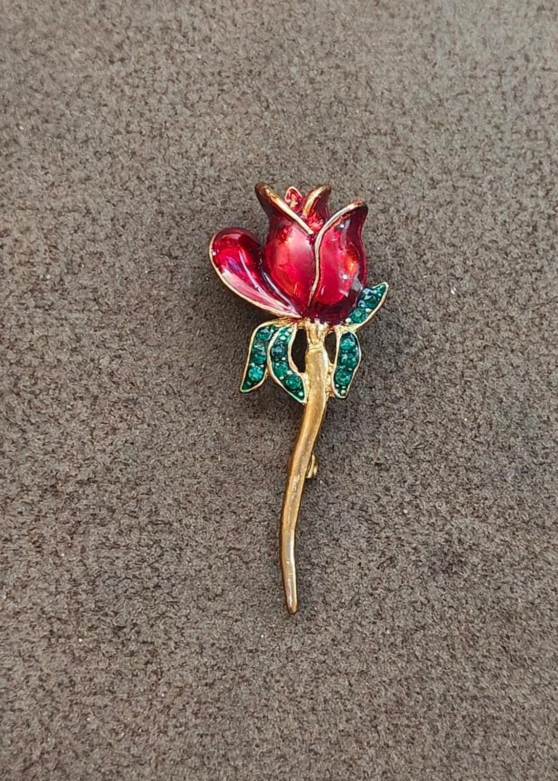 Red enamel flower brooch with green rhinestone leaves and gold-tone stem, flat view