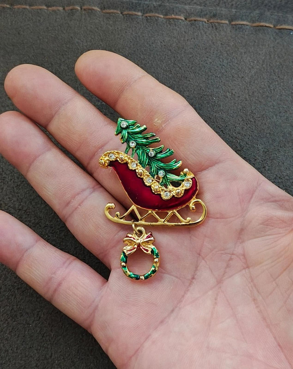 Red sleigh enamel pin with green Christmas tree, gold runners, and hanging wreath charm.