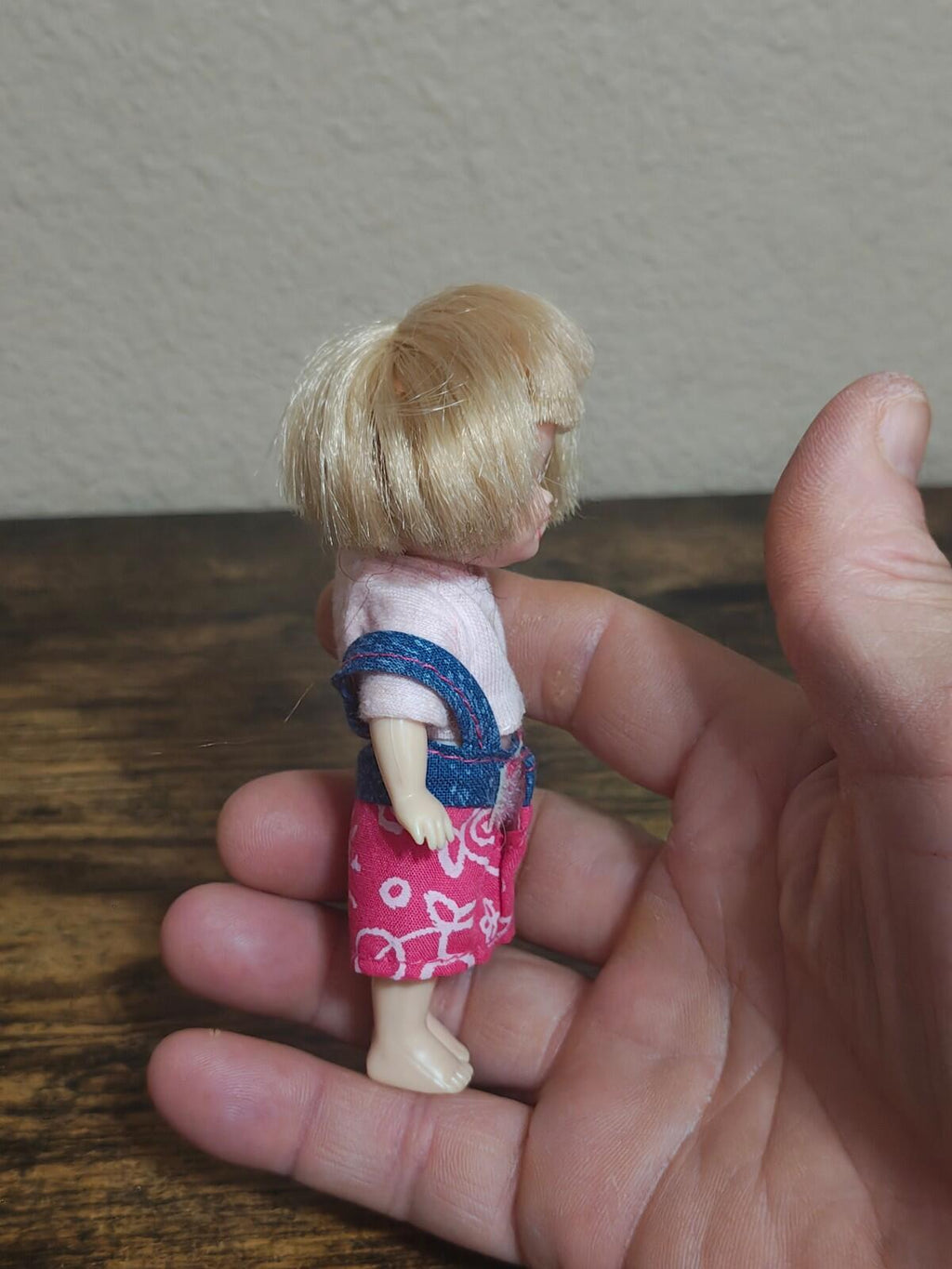 Mini girl doll in hand, side view showing blonde hair and pink patterned shorts