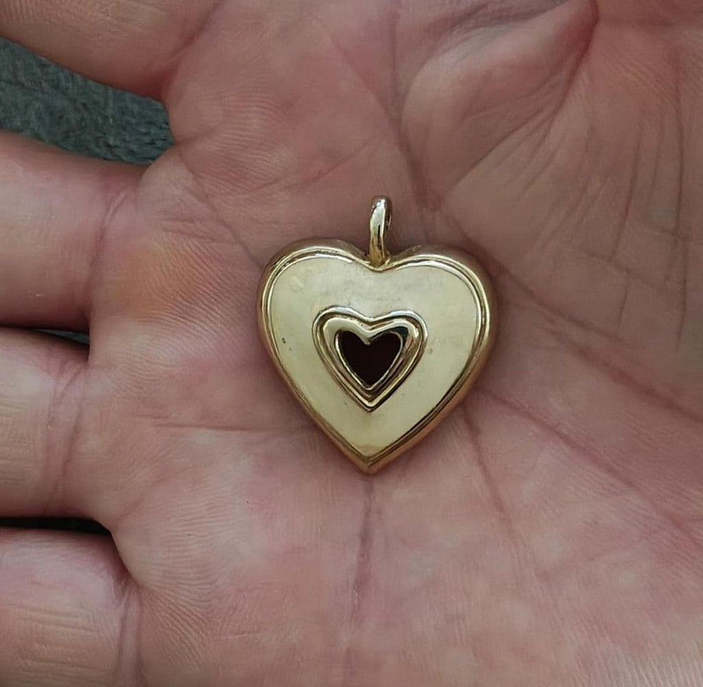 Gold tone heart pendant with white enamel front and black heart center, held in palm
