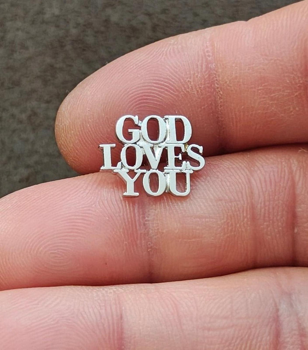 Sterling silver pin with “GOD LOVES YOU” text, close-up on finger
