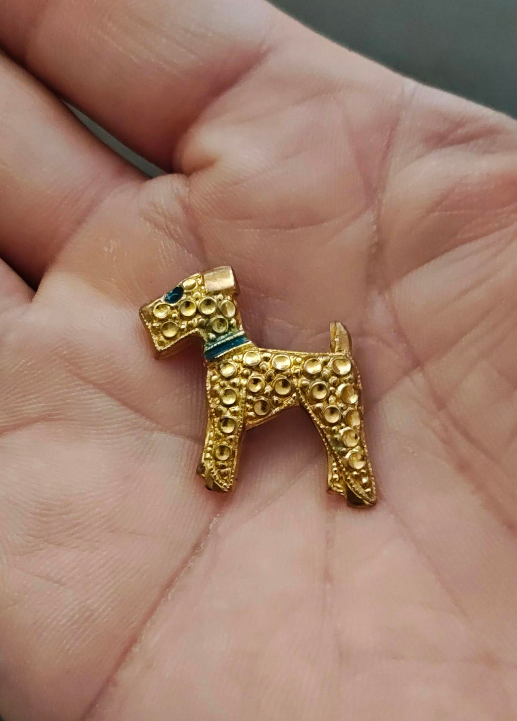 Gold-tone terrier dog brooch with blue enamel band at neck and ornate surface detail.