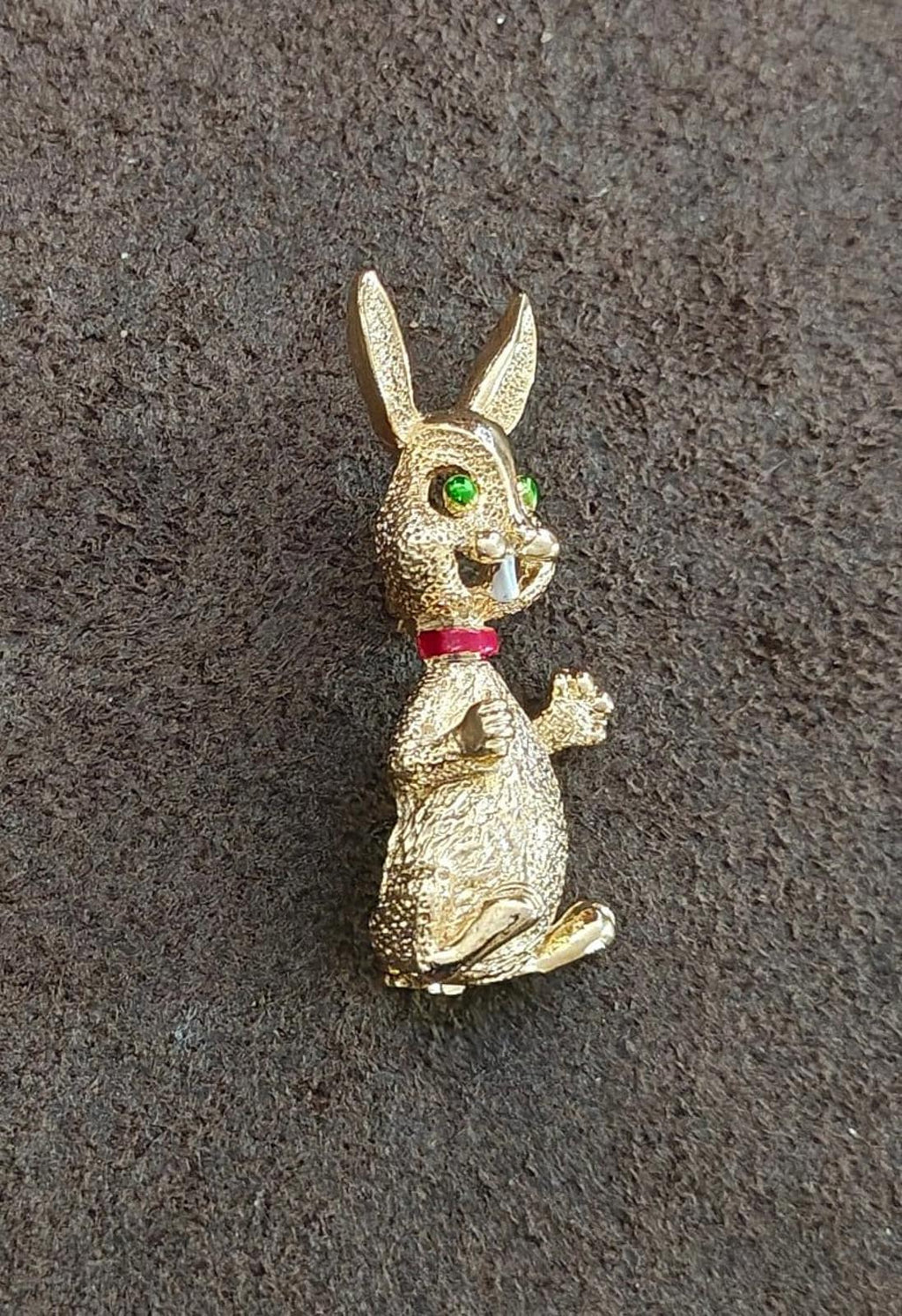 Gold-tone bunny rabbit brooch pin in side profile with green eye enamel and red bow.