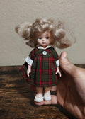 Vintage doll with curly light-brown hair, green plaid dress, white blouse, button