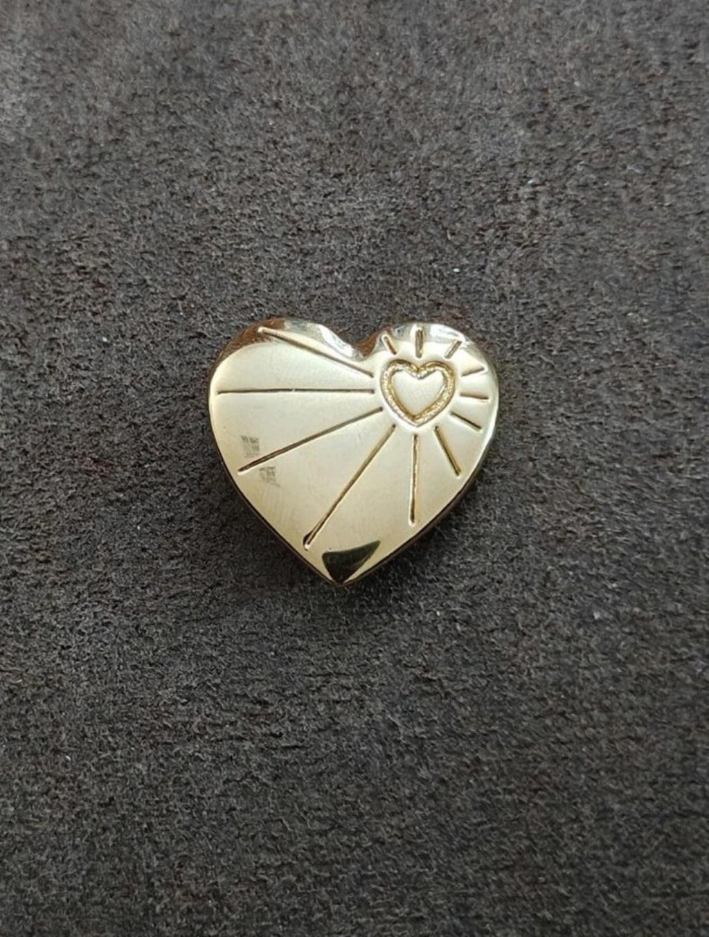 Gold tone heart pin brooch shown on dark fabric with raised rays and inner heart